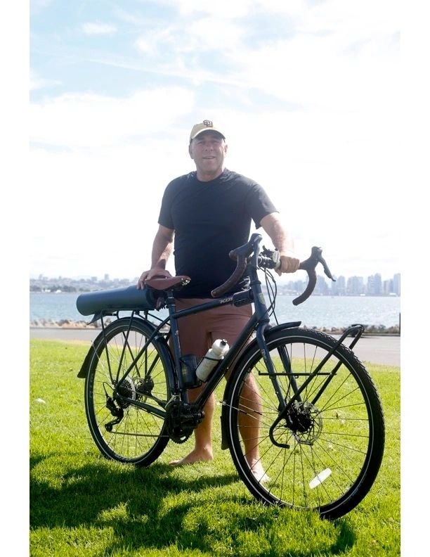 Andy Hanshaw with his bicycle at a waterfront park with city skyline